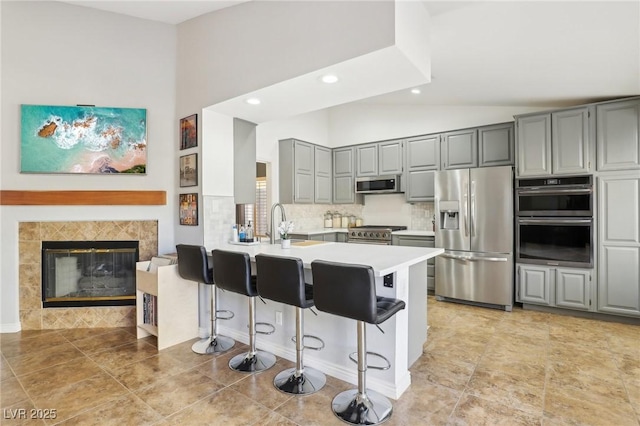 kitchen featuring stainless steel appliances, a tiled fireplace, tasteful backsplash, kitchen peninsula, and a breakfast bar