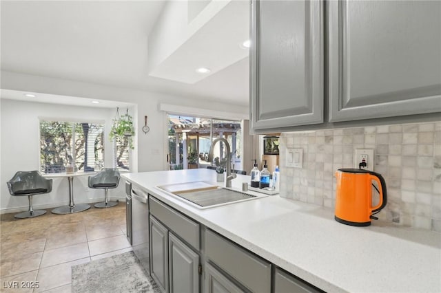 kitchen featuring sink, dishwasher, light tile patterned floors, decorative backsplash, and gray cabinetry