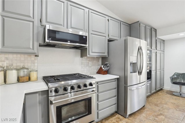 kitchen featuring tasteful backsplash, stainless steel appliances, vaulted ceiling, and gray cabinetry