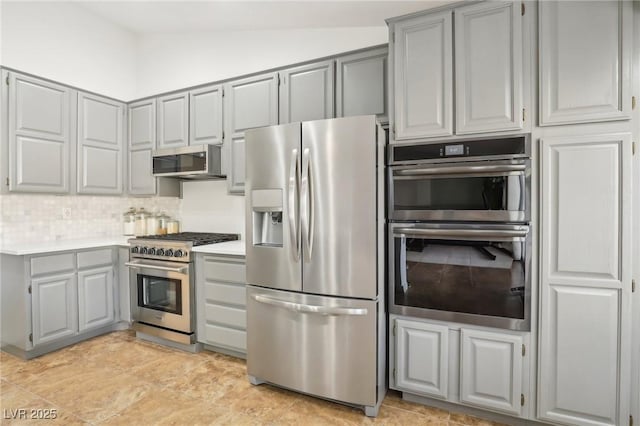 kitchen with appliances with stainless steel finishes, vaulted ceiling, gray cabinetry, and decorative backsplash