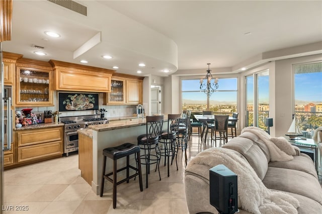 kitchen featuring pendant lighting, high end stainless steel range oven, light stone countertops, a healthy amount of sunlight, and a kitchen bar