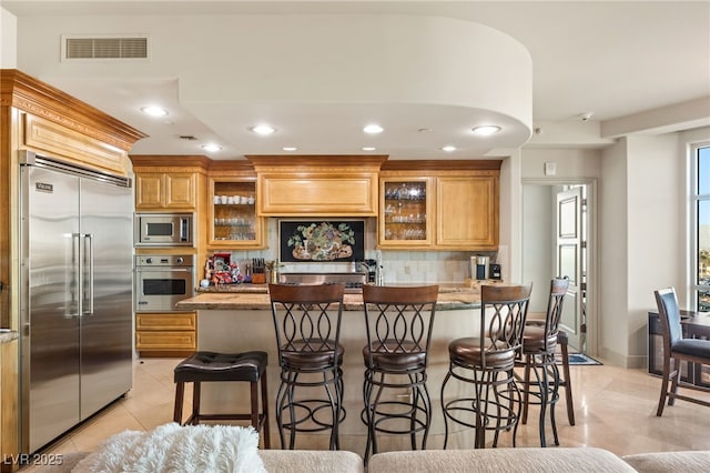 kitchen with built in appliances, light tile patterned floors, tasteful backsplash, and a breakfast bar area