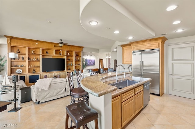 kitchen featuring sink, a breakfast bar area, light stone counters, stainless steel appliances, and a center island with sink