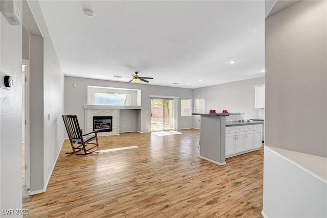 kitchen featuring dark countertops, a glass covered fireplace, white cabinetry, light wood finished floors, and ceiling fan