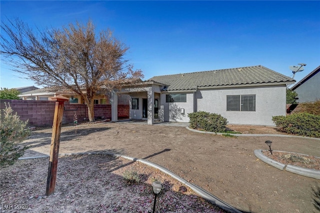 back of house with stucco siding, a tile roof, and fence