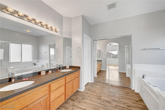 full bath featuring double vanity, wood finished floors, visible vents, and a sink