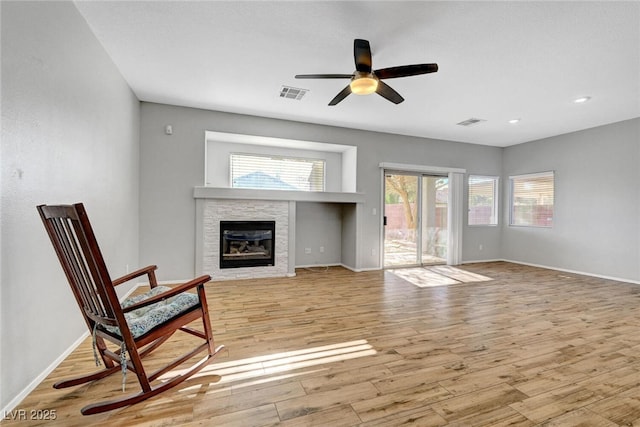 living area featuring light wood-type flooring, visible vents, a ceiling fan, a fireplace, and baseboards