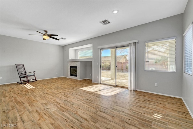 unfurnished living room featuring visible vents, a glass covered fireplace, a ceiling fan, and light wood finished floors