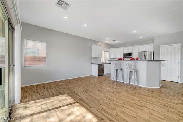 kitchen featuring tasteful backsplash, visible vents, light wood-type flooring, stainless steel appliances, and white cabinetry