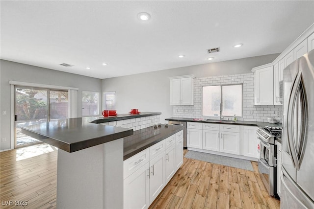 kitchen featuring dark countertops, backsplash, appliances with stainless steel finishes, and light wood-style floors