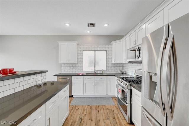 kitchen featuring visible vents, appliances with stainless steel finishes, white cabinetry, dark countertops, and light wood-type flooring