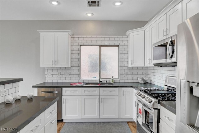 kitchen with dark countertops, visible vents, appliances with stainless steel finishes, white cabinetry, and a sink