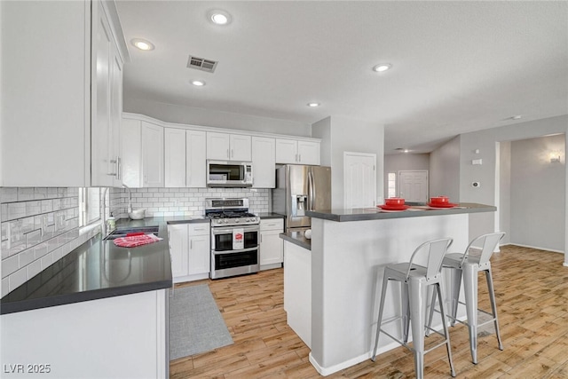 5919 Pavilion Lakes Ave, Las Vegas, NV 89122 - kitchen with appliances with stainless steel finishes, dark countertops, light wood-style floors, white cabinetry, and a breakfast bar area