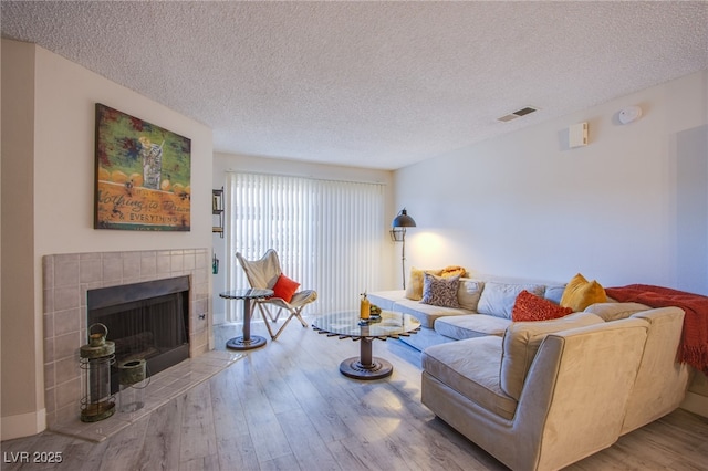 living room featuring a tile fireplace, a textured ceiling, and hardwood / wood-style flooring