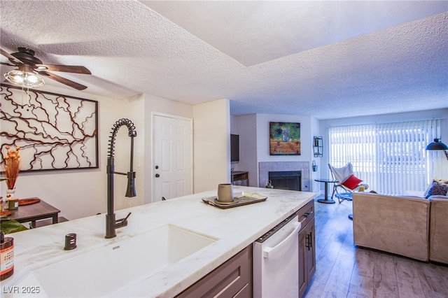 kitchen featuring ceiling fan, sink, stainless steel dishwasher, a textured ceiling, and a tiled fireplace