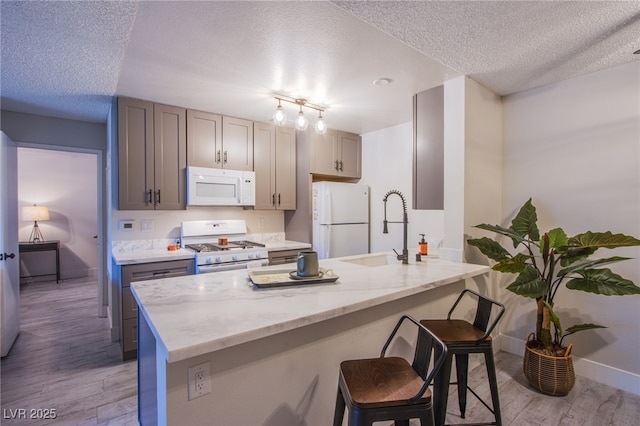 kitchen with sink, light hardwood / wood-style floors, a textured ceiling, white appliances, and gray cabinets