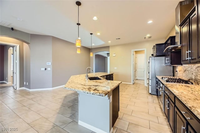 kitchen with a kitchen island with sink, sink, light stone countertops, and decorative light fixtures