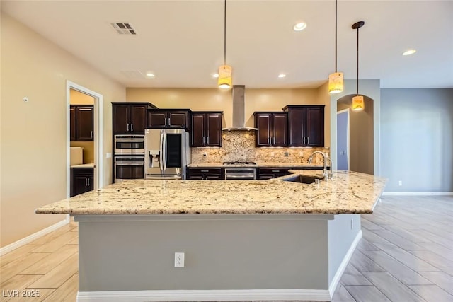 kitchen featuring appliances with stainless steel finishes, sink, wall chimney range hood, hanging light fixtures, and a large island