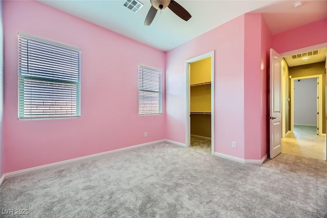 unfurnished bedroom with ceiling fan, a walk in closet, light carpet, and a closet