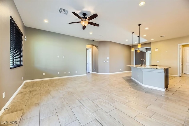 kitchen with a kitchen island with sink, ceiling fan, light stone counters, and decorative light fixtures