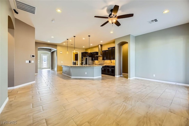 kitchen with backsplash, a kitchen island with sink, ceiling fan, stainless steel fridge, and decorative light fixtures