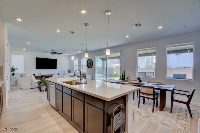 kitchen with sink, hanging light fixtures, light hardwood / wood-style flooring, ceiling fan, and an island with sink