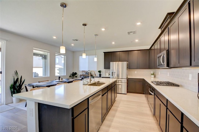 kitchen featuring sink, an island with sink, pendant lighting, dark brown cabinets, and appliances with stainless steel finishes