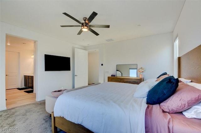 bedroom featuring light colored carpet, ensuite bath, and ceiling fan