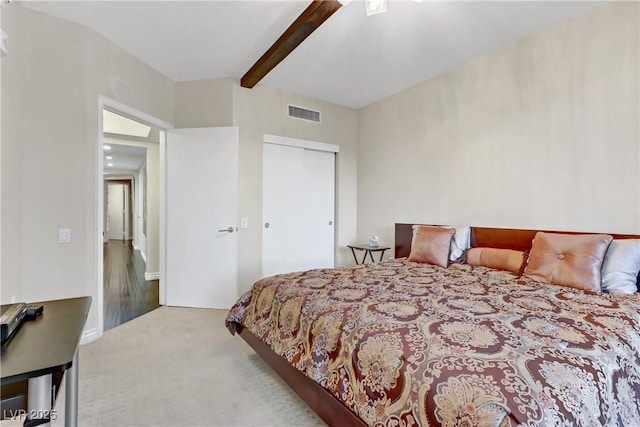 bedroom with beamed ceiling, ceiling fan, light colored carpet, and a closet