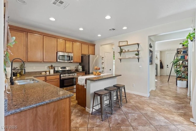 kitchen featuring stainless steel appliances, sink, dark stone countertops, a kitchen island, and a breakfast bar area