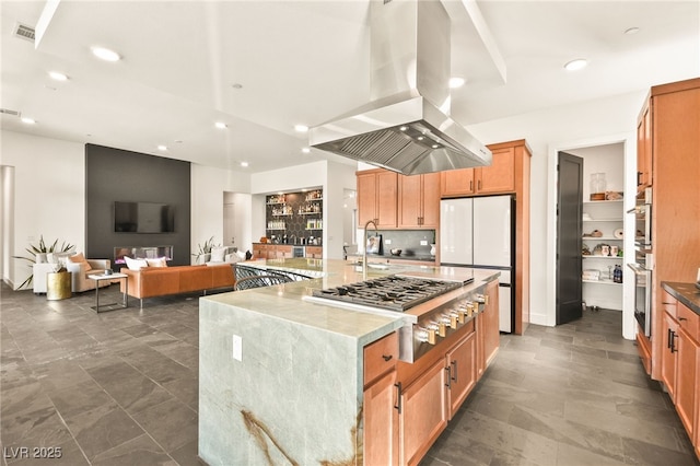 kitchen with light stone counters, white fridge, a spacious island, stainless steel gas stovetop, and island range hood