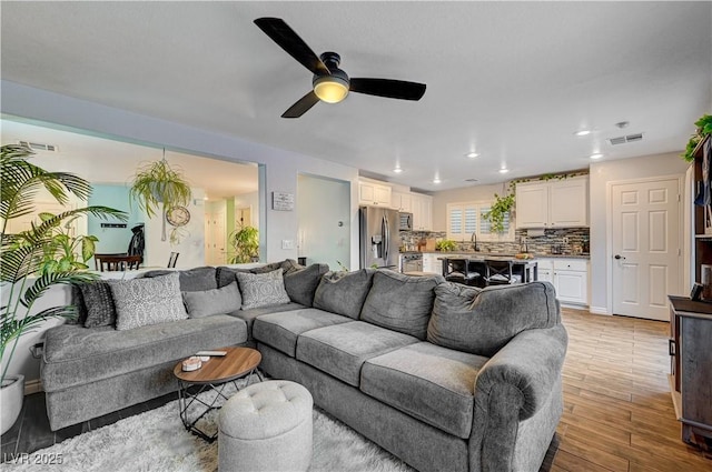 living room with light hardwood / wood-style floors, ceiling fan, and sink