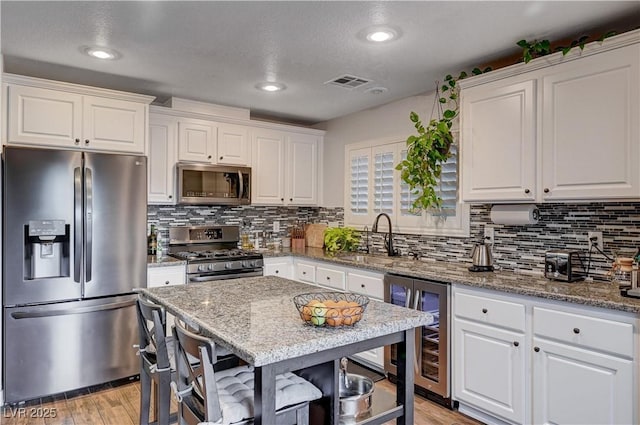 kitchen with white cabinetry, sink, beverage cooler, stainless steel appliances, and light stone counters