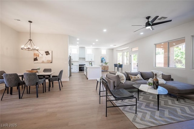 living room with ceiling fan with notable chandelier, light hardwood / wood-style floors, and sink