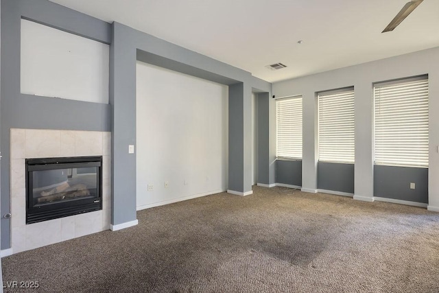 unfurnished living room with a tiled fireplace, ceiling fan, and carpet