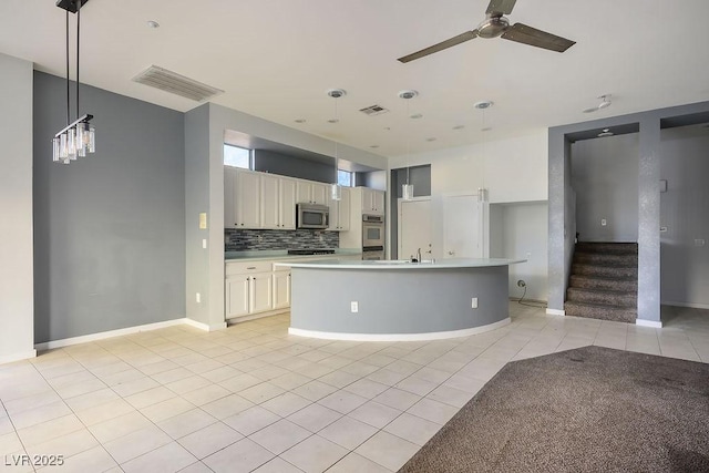 kitchen with appliances with stainless steel finishes, ceiling fan, light tile patterned floors, pendant lighting, and a center island with sink