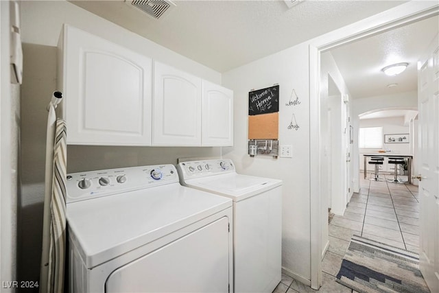 washroom featuring washer and dryer, cabinets, light tile patterned floors, and a textured ceiling