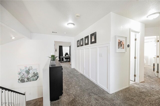 corridor with a textured ceiling and dark colored carpet