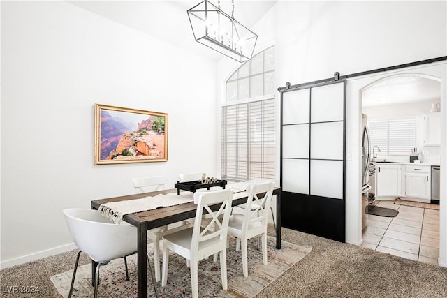 dining room featuring sink, light carpet, a barn door, and a chandelier