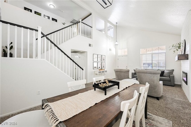 carpeted dining area with a towering ceiling and a large fireplace