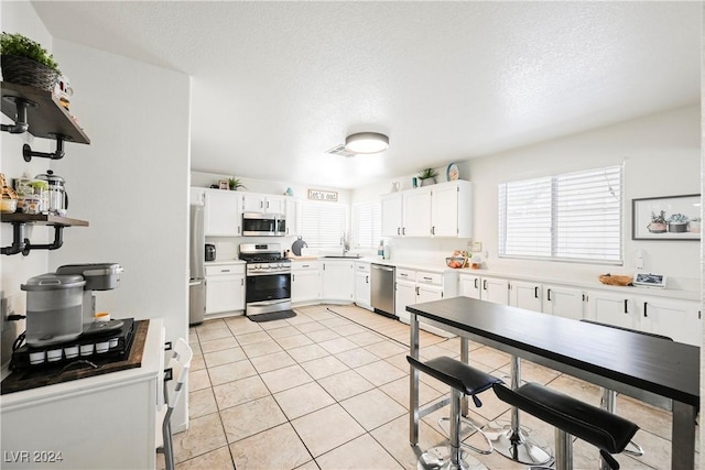 kitchen featuring a textured ceiling, stainless steel appliances, white cabinetry, and light tile patterned flooring