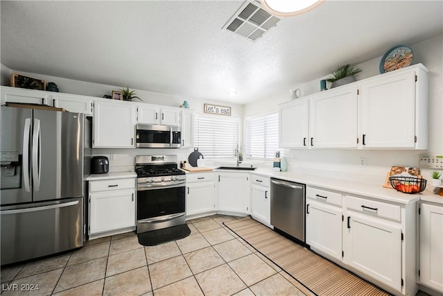 kitchen featuring stainless steel appliances, sink, white cabinetry, a textured ceiling, and light tile patterned flooring