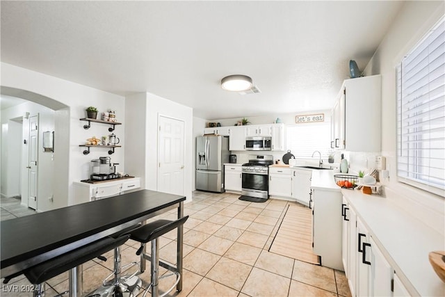 kitchen featuring appliances with stainless steel finishes, light tile patterned floors, a healthy amount of sunlight, white cabinets, and sink