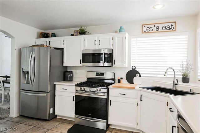 kitchen featuring sink, appliances with stainless steel finishes, light tile patterned floors, and white cabinetry