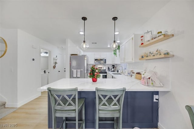 kitchen featuring a breakfast bar, kitchen peninsula, sink, appliances with stainless steel finishes, and white cabinetry