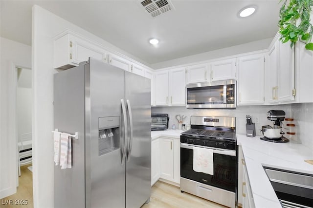 kitchen featuring decorative backsplash, appliances with stainless steel finishes, sink, white cabinets, and light hardwood / wood-style floors