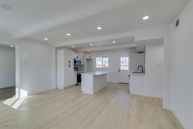 kitchen featuring a center island, sink, appliances with stainless steel finishes, beam ceiling, and white cabinetry