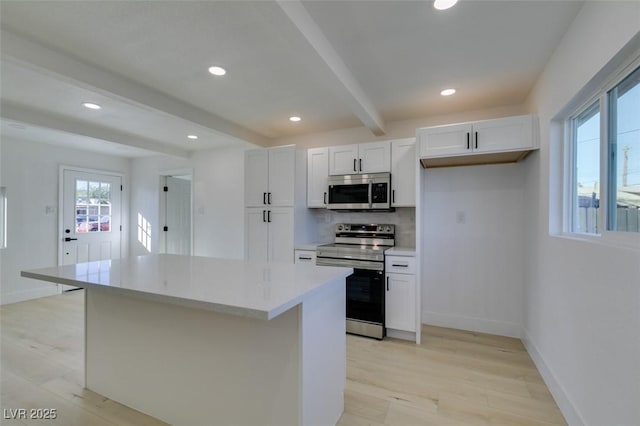 kitchen with beamed ceiling, stainless steel appliances, a kitchen island, and white cabinetry