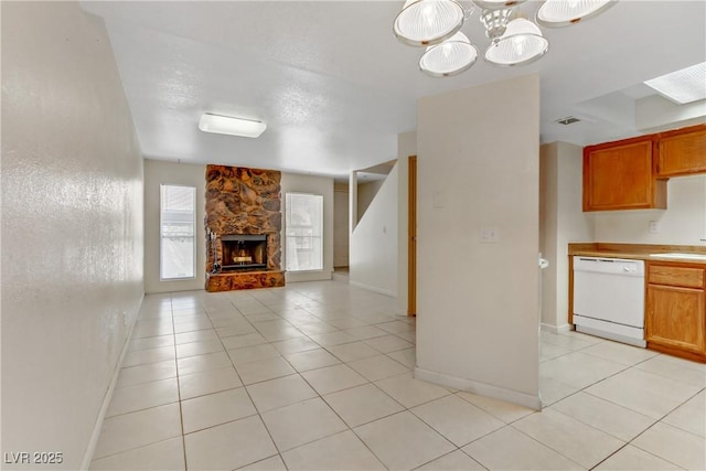 unfurnished living room featuring a stone fireplace, sink, light tile patterned floors, and a notable chandelier