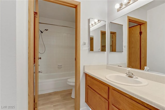 full bathroom with hardwood / wood-style floors, vanity, tiled shower / bath combo, and toilet